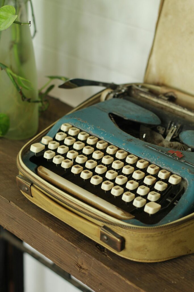 A classic blue typewriter sits in a vintage carrying case on a wooden surface with soft lighting.